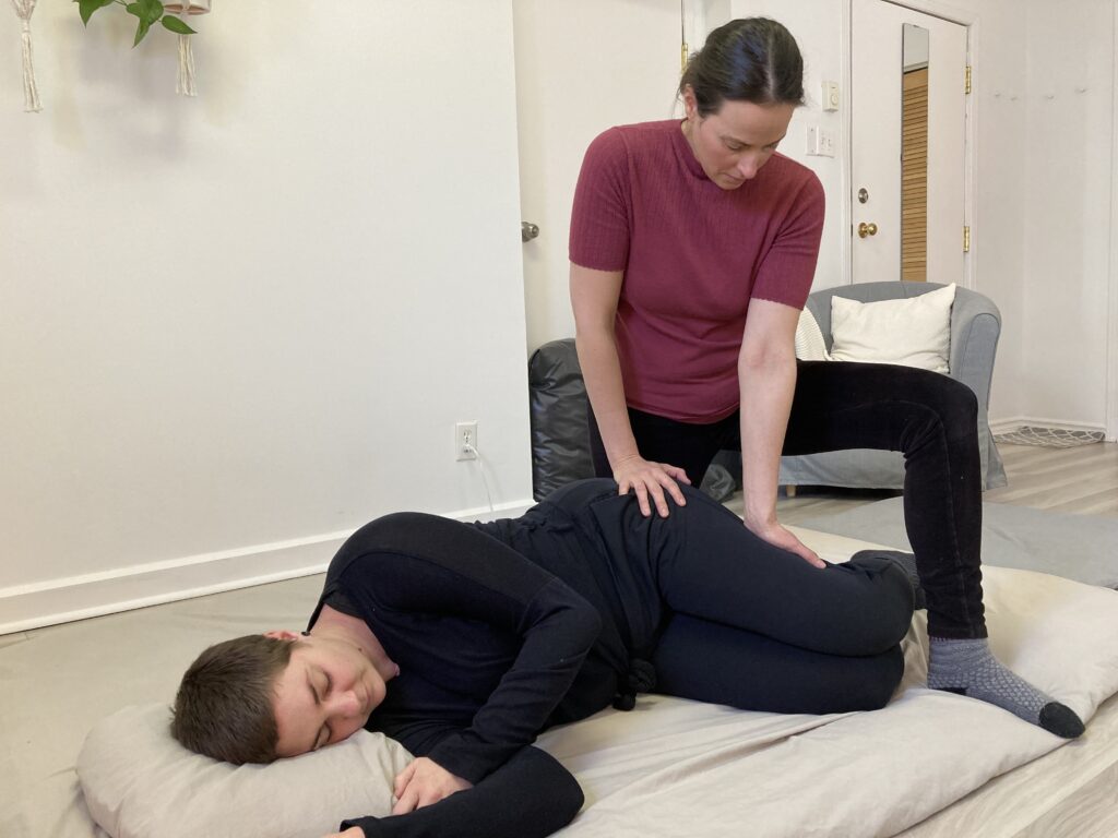 Photo de Patsy qui effectue des pressions sur les membres inférieurs sur un receveur habillé et installé en position latérale sur un futon de Shiatsu.